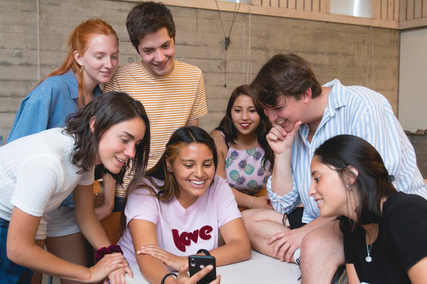 Grupo de jóvenes riendo y mirando un teléfono juntos en una sala.