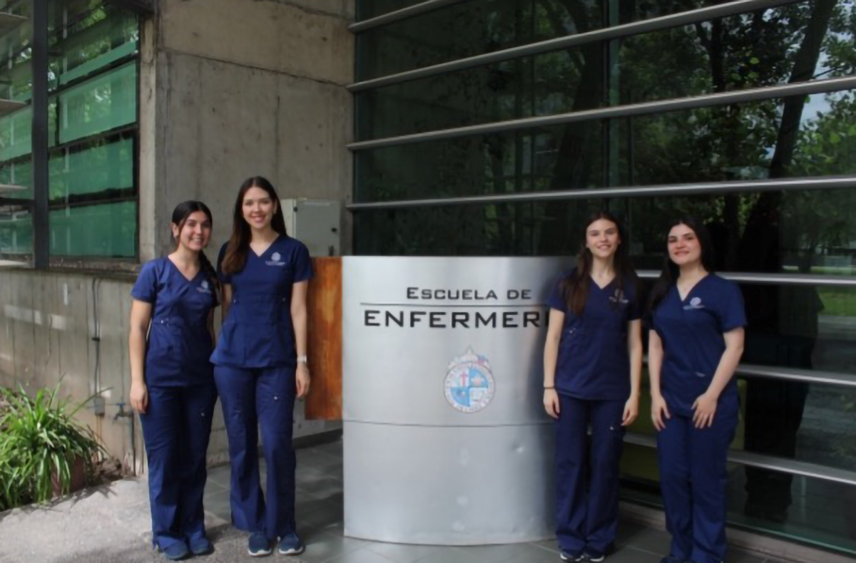 Cuatro enfermeras en uniforme junto a un cartel de la Escuela de Enfermería.